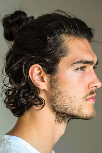 Penteado de coque encurreado meio para baixo, um homem com cabelos castanhos escuros, vista lateral.