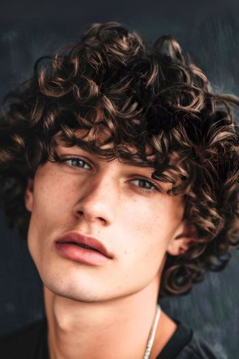 Penteado de corte de tigela encaracolada em um homem com cabelos castanhos.