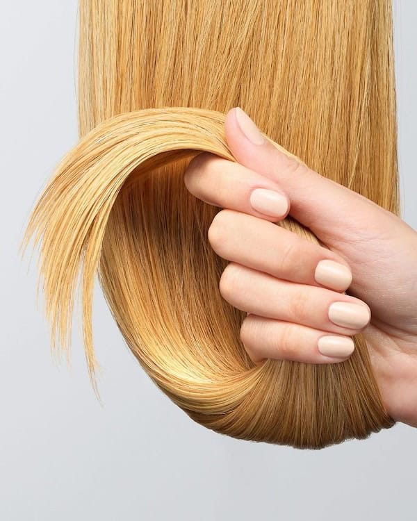 Mão segurando longos cabelos loiros de morango.