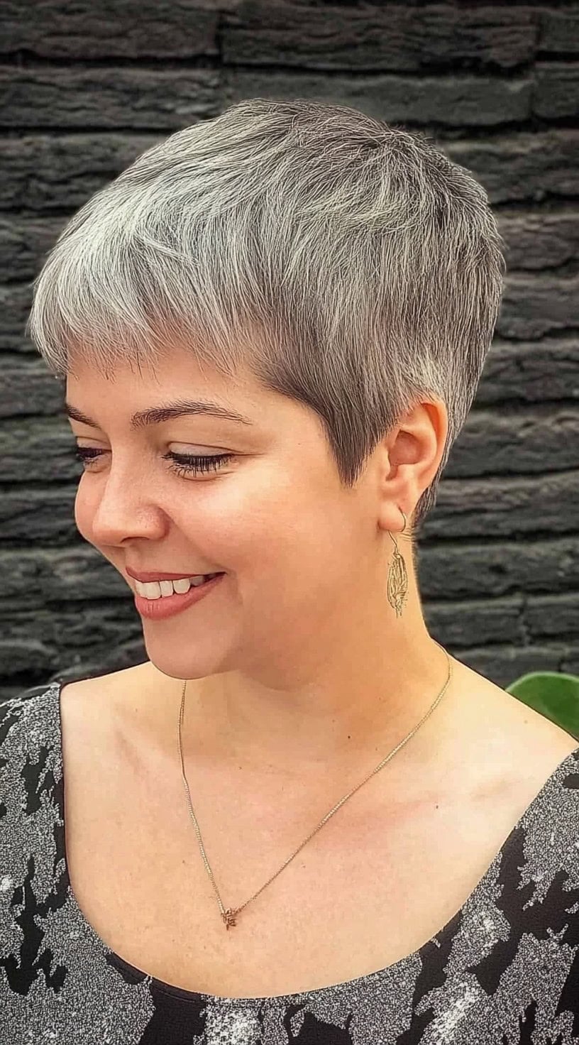 Uma mulher com um corte de pixie cinza prateado e bordas arredondadas, sorrindo enquanto se virou levemente para o lado.