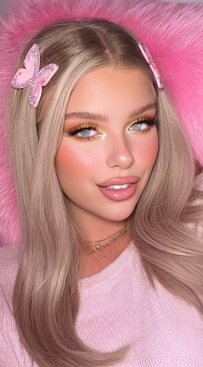 Uma mulher com cabelos loiros longos e elegantes, separados no meio, acessórios com clipes de borboleta de strass rosa de cada lado.